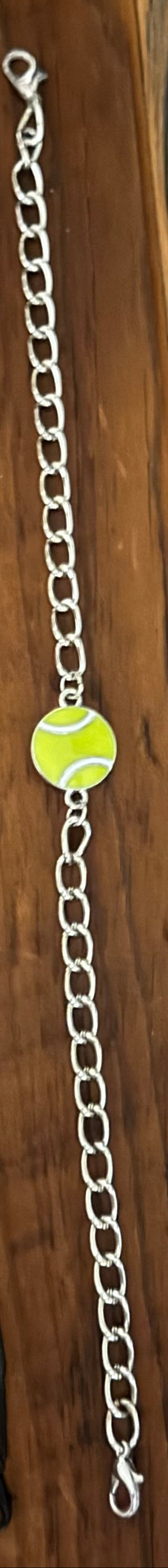 Two tennis-themed bracelets displayed on a wooden surface. One bracelet features a black metal chain with two round lime-green tennis ball charms.
