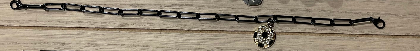 A black metal link chain bracelet with a small silver-toned skull charm, laid flat on a light wood surface.