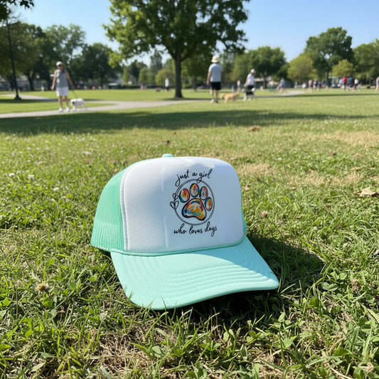 A mint green and white trucker hat with a colorful paw print graphic and the text 'just a girl who loves dogs' on the front panel.