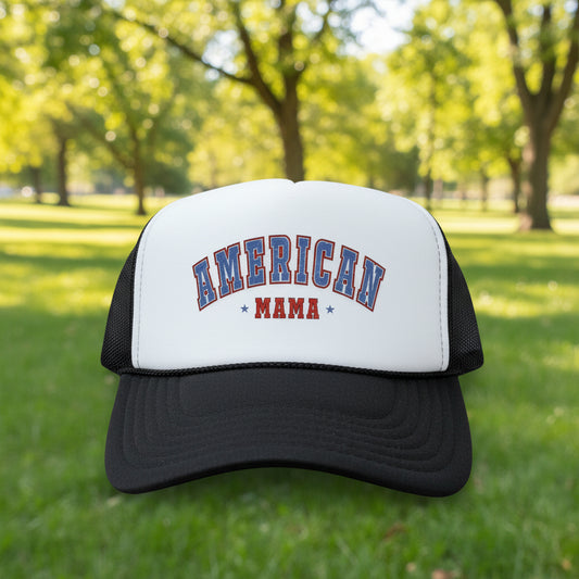 A white and black trucker hat with 'AMERICAN MAMA' printed on the front panel, resting on a wooden surface.
