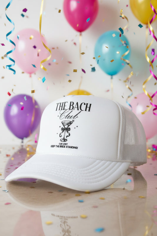 A white trucker hat with black text reading 'THE BACH Club' .