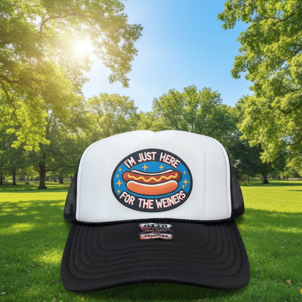 A black and white trucker hat with a circular patch on the front that reads 'I'M JUST HERE FOR THE WEINERS' around a hot dog illustration. The hat has a white front panel, black mesh back, and black brim, with a visible 'Made in USA' sticker on the brim.