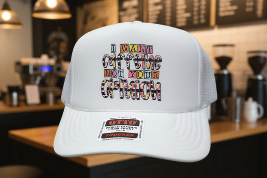 A white trucker hat with a foam front panel and mesh side/back panels. The front has a large rectangular graphic with the phrase “I WANT COFFEE NOT YOUR OPINION” in multicolored block letters.