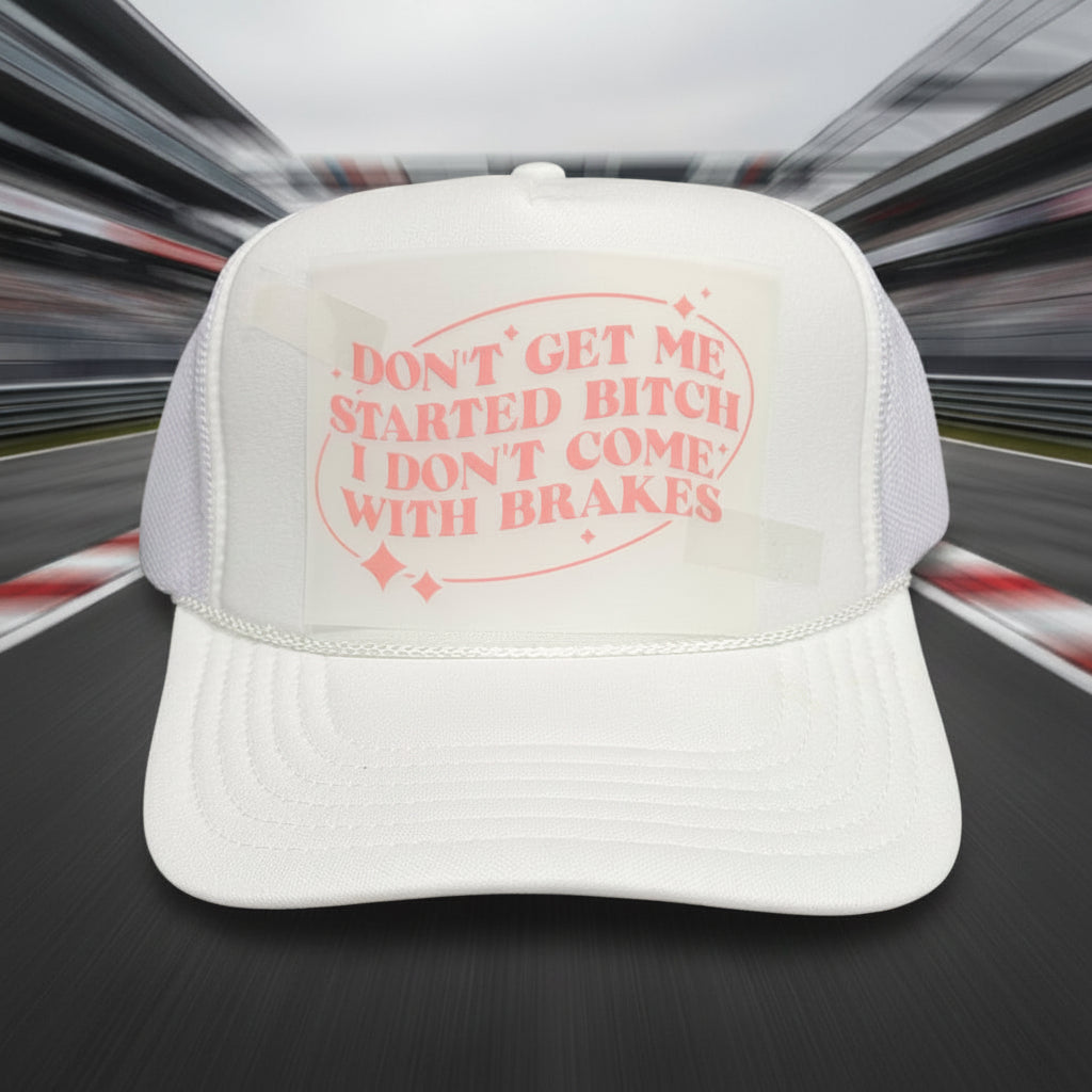 A white trucker hat with a pink graphic on the front that reads 'DON'T GET ME STARTED BITCH I DON'T COME WITH BRAKES' and a visible Otto brand sticker on the brim, set against a dark wood background.