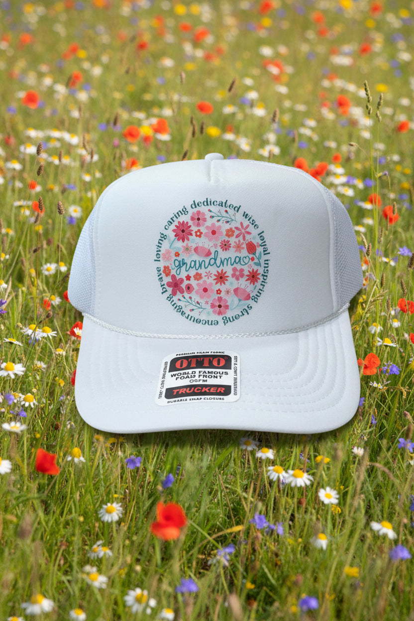A white trucker hat with a floral 'Grandma' graphic on the front panel, resting on a wooden surface. The sticker on the brim identifies the brand as Otto Trucker.