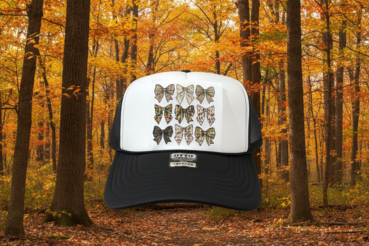 A black and white trucker hat with a graphic of twelve bow designs on the front panel, displayed on a rustic wooden surface.