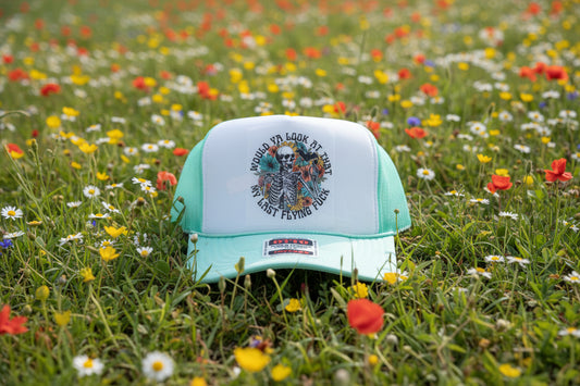 A mint green and white trucker hat with a graphic print of a skeleton and flowers on the front panel.