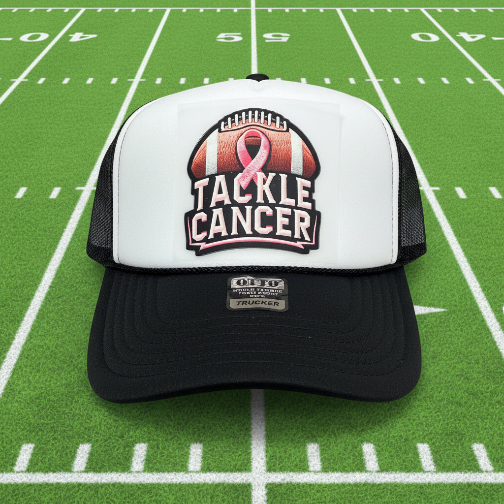 A black and white trucker hat featuring a front patch that reads 'TACKLE CANCER' with a pink ribbon over a football graphic. The brim has a visible 'OF-TO World Famous Foam Front Trucker' patch.