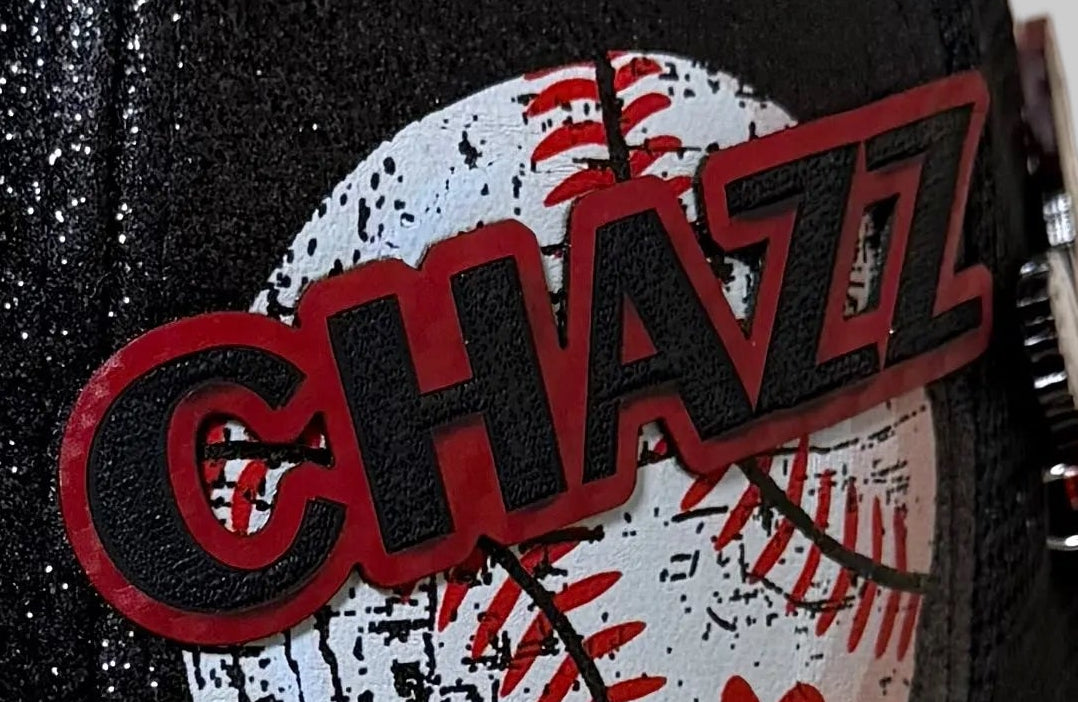 A black glitter baseball cap with a baseball-themed beaded chain, a baseball patch, and a custom photo insert, displayed alongside a black chain accessory with a red bird charm on a beige background.