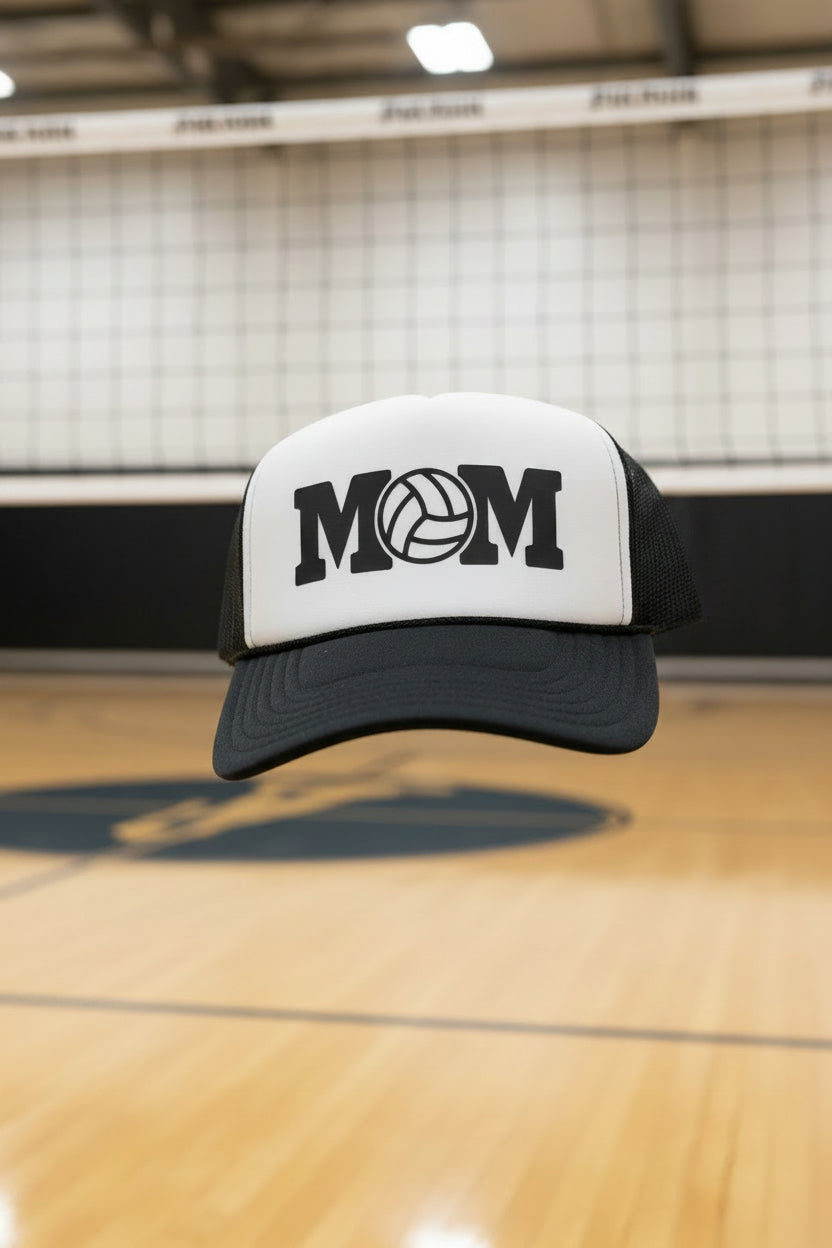 A black and white trucker hat with 'MOM' and a volleyball graphic on the front