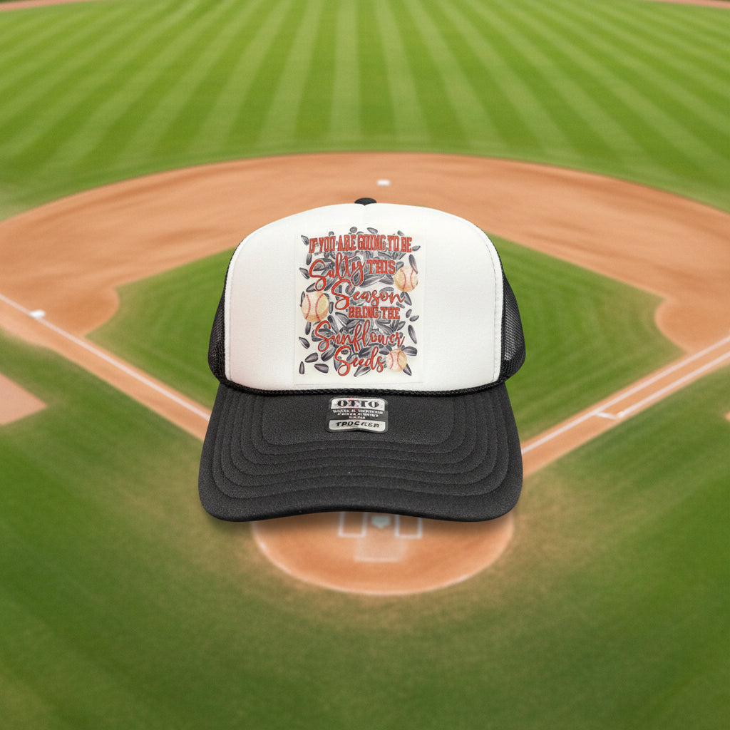 A white and dark gray trucker hat with a custom graphic on the front. The graphic features the text 'If You Are Going To Be Salty this Season bring The Sunflower Seeds' in orange and gray lettering, decorated with illustrations of baseballs and sunflower seeds.