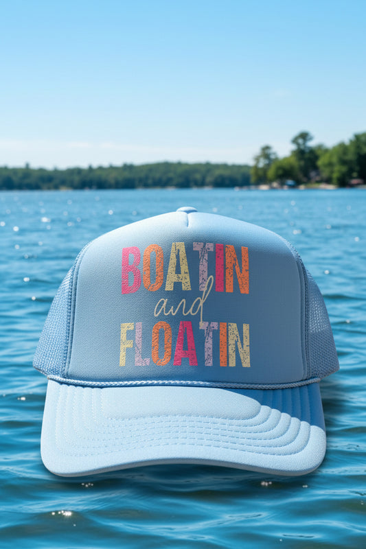 A light blue trucker hat with a large clear vinyl decal reading 'BOATIN and FLOATIN' in multicolored letters. The hat has a visible Otto Trucker sticker on the front foam panel.