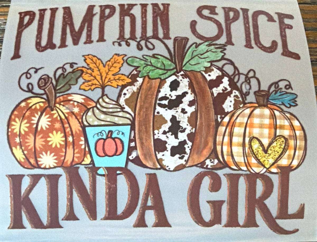A square white sticker or decal with a fall-themed illustration and the text 'PUMPKIN SPICE KINDA GIRL' in brown lettering, placed on a wooden surface.