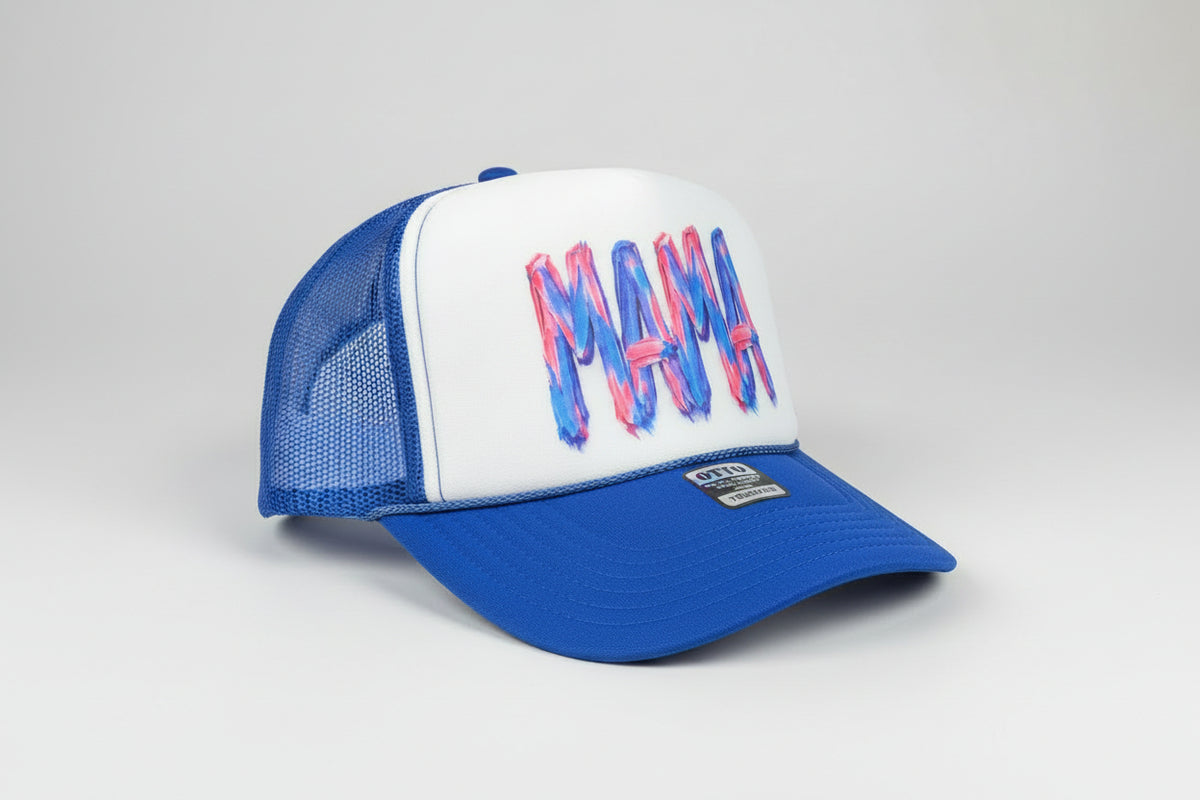 A blue and white trucker hat with the word 'MAMA' written across the front in a pink and blue brushstroke style. The brim is bright blue, and the mesh back is also blue.