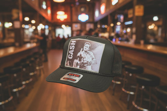 A dark gray trucker hat with a front graphic DTF patch of Johnny Cash and the word 'CASH' in white. 