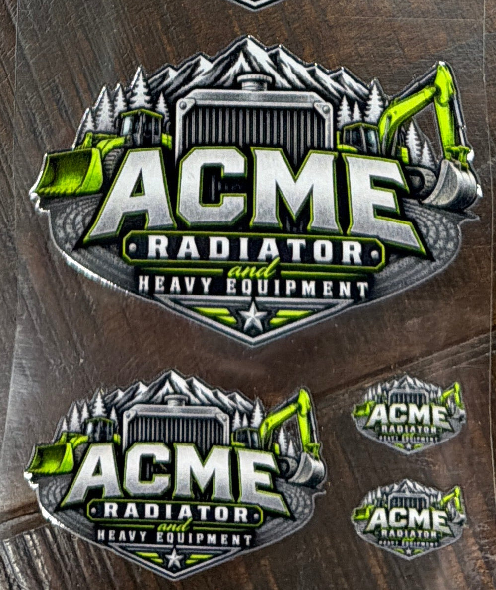 Several clear plastic sleeves containing oval ACME Radiator stickers are arranged on a dark wood surface. The stickers feature a metallic silver and black mountain-style emblem with bright green accents and the text 'ACME RADIATOR' and 'HIGH PERFORMANCE'.