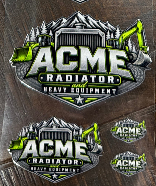 Several clear plastic sleeves containing oval ACME Radiator stickers are arranged on a dark wood surface. The stickers feature a metallic silver and black mountain-style emblem with bright green accents and the text 'ACME RADIATOR' and 'HIGH PERFORMANCE'.