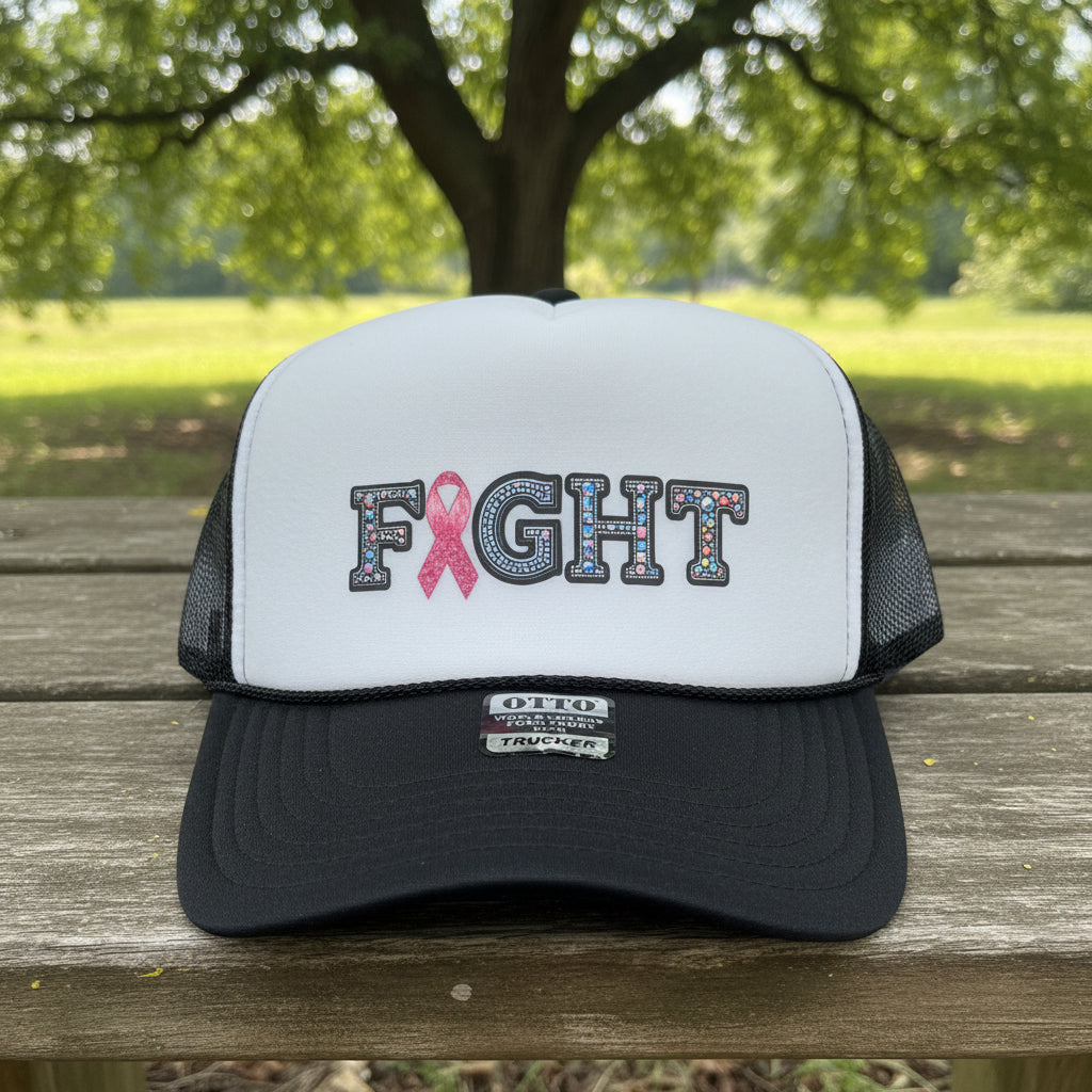 A white and black trucker hat with 'FIGHT' lettering on the front, where the 'I' is replaced by a pink ribbon. The hat has a white front panel, black mesh back, and a black brim with a visible 'OTTO' brand tag.