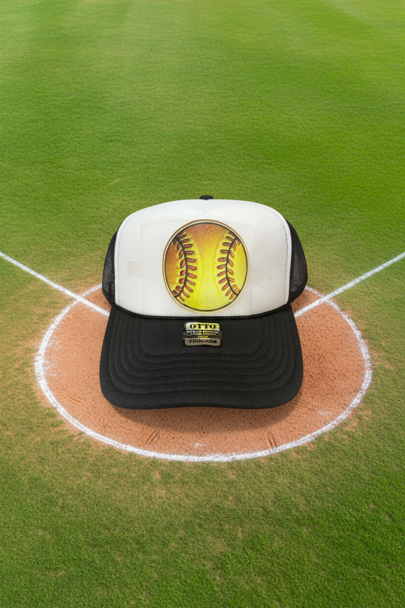 A black and white trucker hat featuring a custom printed yellow softball graphic on the front panel. The hat has a black visor with a gold-tone 'OTTO TRUCKER' brand patch and black mesh side panel.