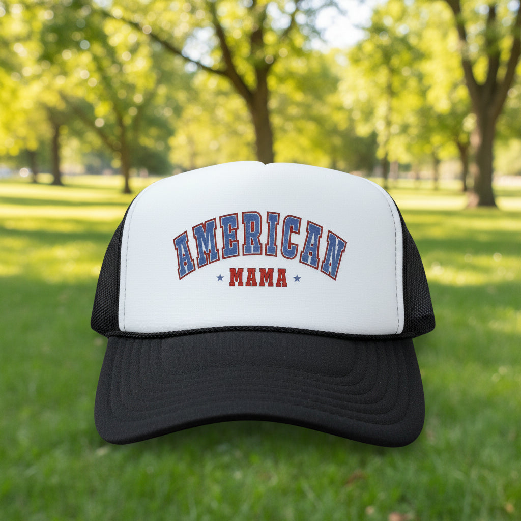 A white and black trucker hat with 'AMERICAN MAMA' printed on the front panel, resting on a wooden surface.
