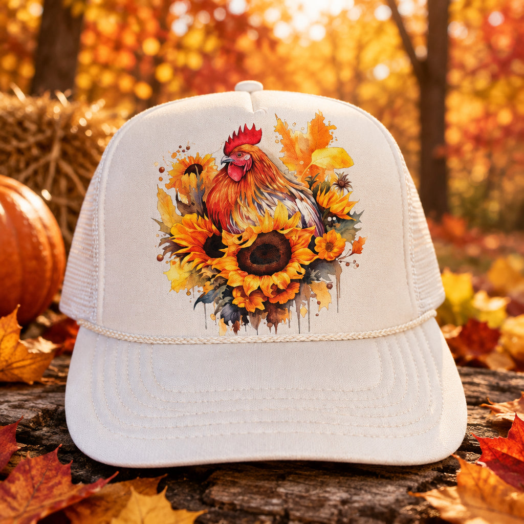 A white trucker hat with a colorful graphic of a rooster and sunflowers on the front panel, resting on a dark wooden surface. The hat features a visible 'OTTO' sticker on the brim.