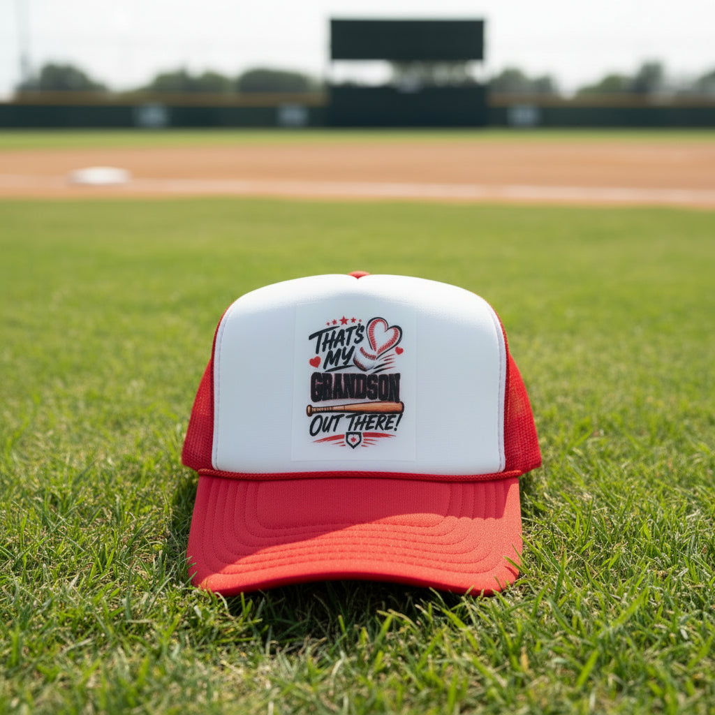 A red and white trucker hat with a custom graphic on the front panel that reads 'THAT'S MY GRANDSON OUT THERE!' with a heart and bat design. The brim has a visible OTTO foam patch.