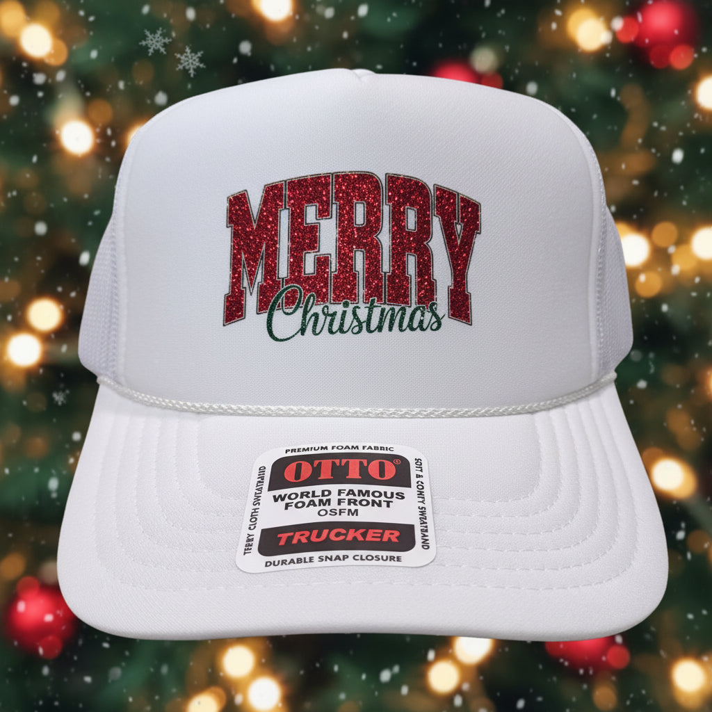 A white trucker-style baseball cap with 'MERRY Christmas' on the front, displayed on a wooden table. The cap features a red and black patterned 'MERRY' text with 'Christmas' in black cursive underneath.
