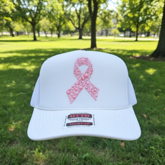 A white foam trucker hat with a pink awareness ribbon on the front, made of patterned pink foam. The hat has white mesh side/back panels and a visible 'OTTO' brand sticker on the brim.