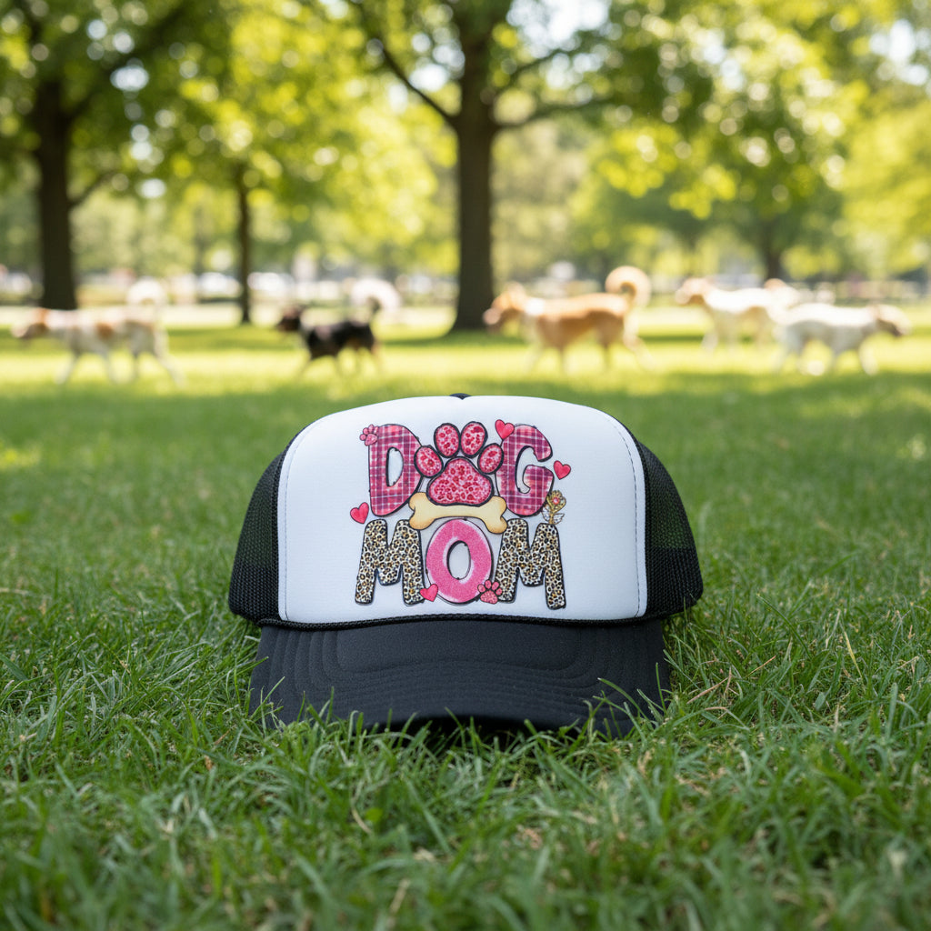 A black and white trucker hat with a custom graphic on the front panel spelling 'DOG MOM' in pink, leopard print, and plaid patterns.