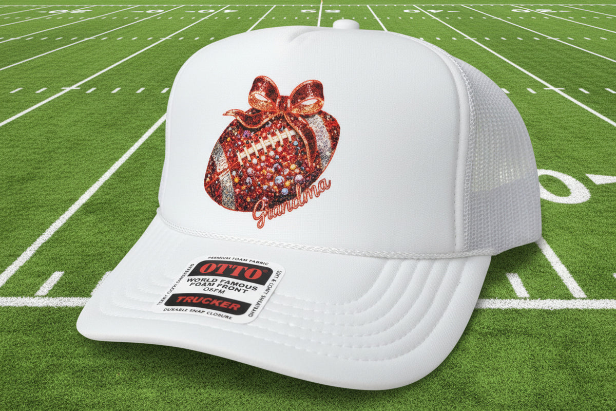 A white foam trucker hat with a custom glittery football patch on the front and a visible Otto Trucker sticker on the brim, set on a wooden surface.