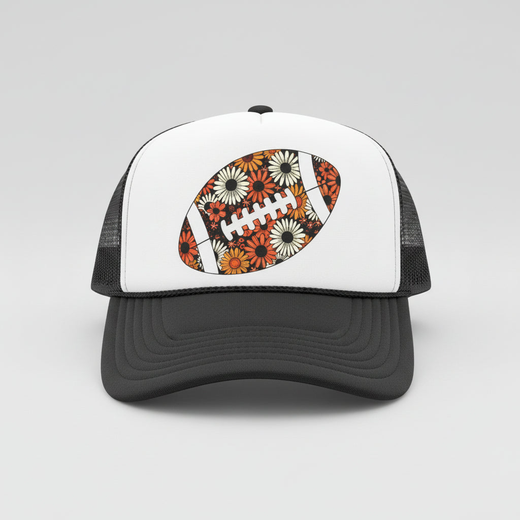 A dark gray and white trucker hat with a floral football graphic on the front, resting on a dark wooden table against a wood-paneled background.