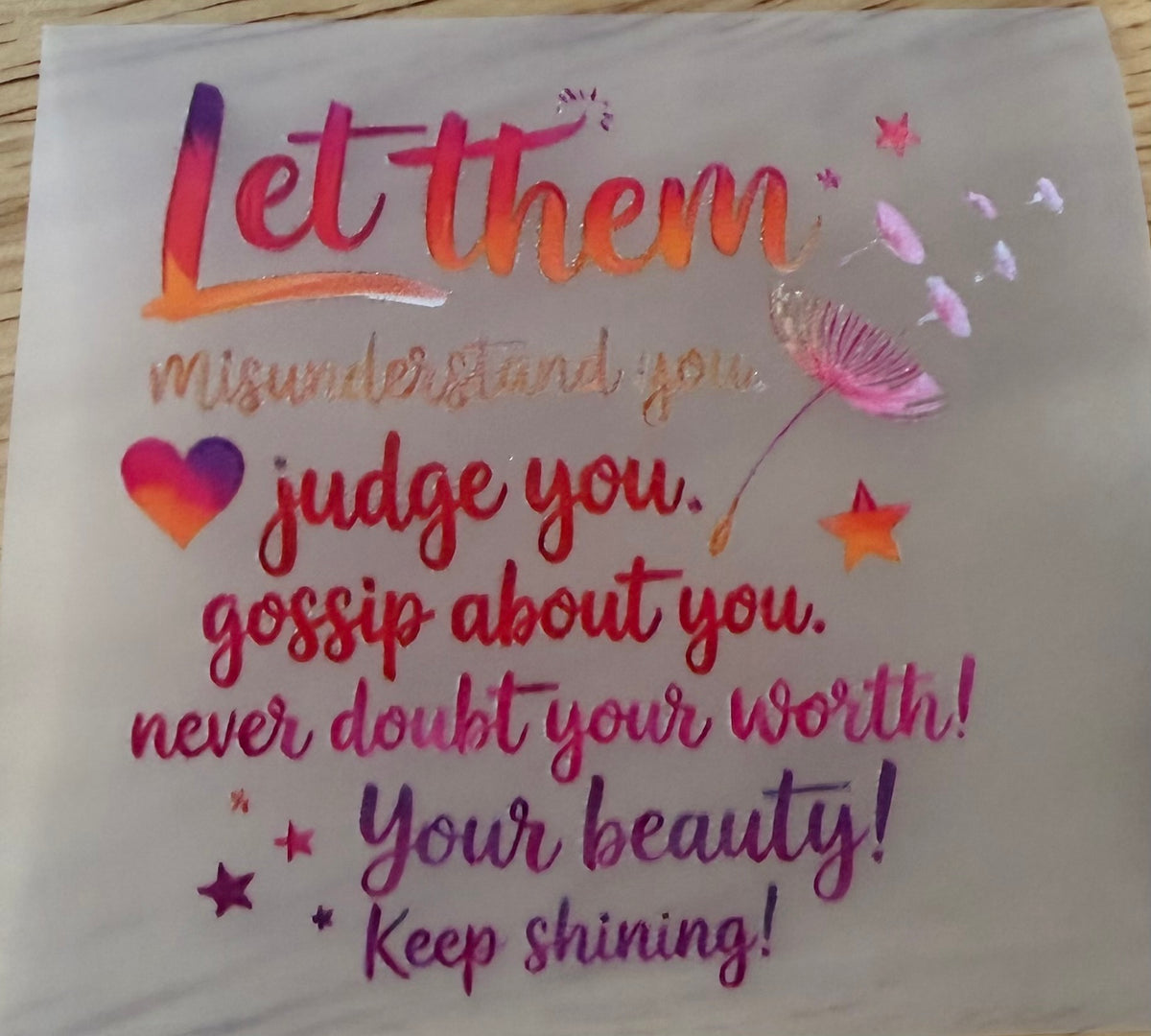 A square white fabric item, likely a napkin or small tablecloth, printed with a colorful inspirational quote. The text reads 'Let them misunderstand you.