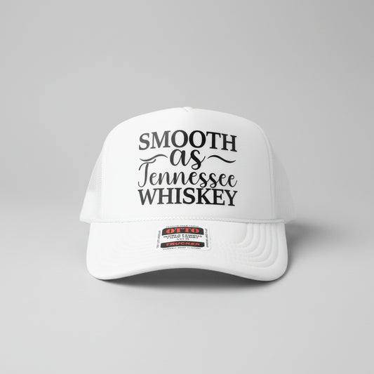 A white foam trucker hat with black text reading 'SMOOTH as Tennessee WHISKEY' on the front panel, photographed on a wooden surface. A visible patch on the brim reads Otto Trucker.