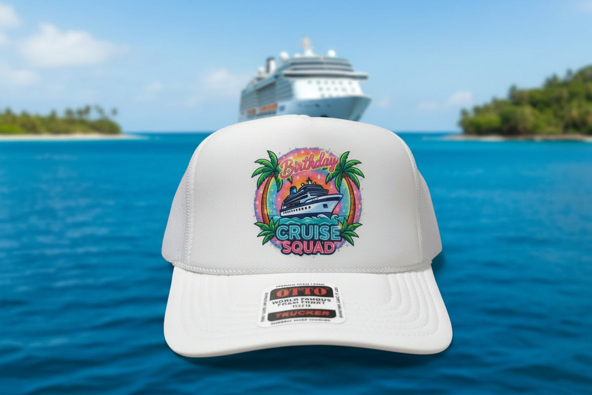 A white trucker hat with a colorful 'Cruise Squad Birthday' cruise ship graphic on the front, resting on a wooden table.