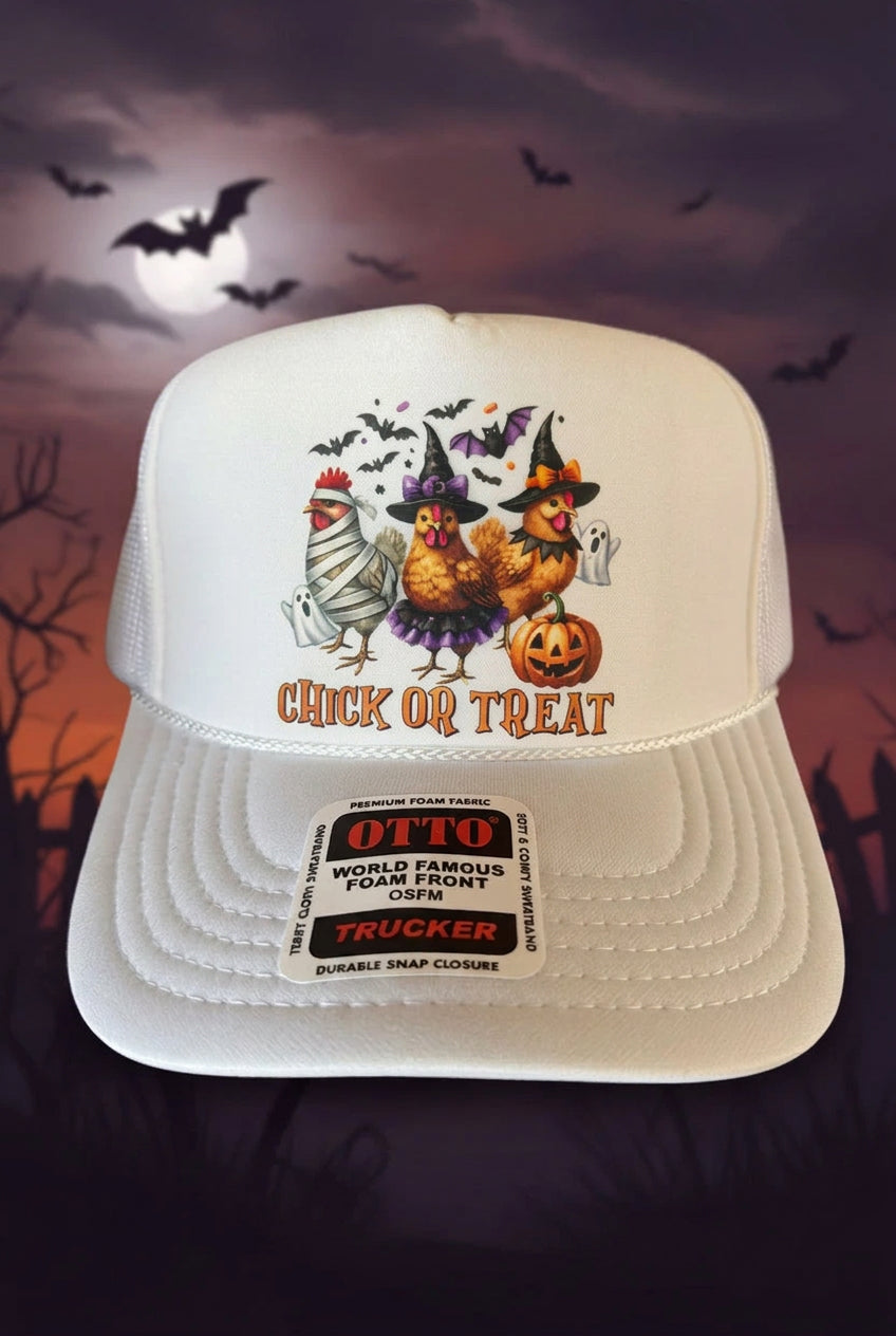A white trucker hat with a Halloween-themed chicken graphic and the text 'CHICK OR TREAT' on the front, shown against a spooky night background with bats and a full moon.