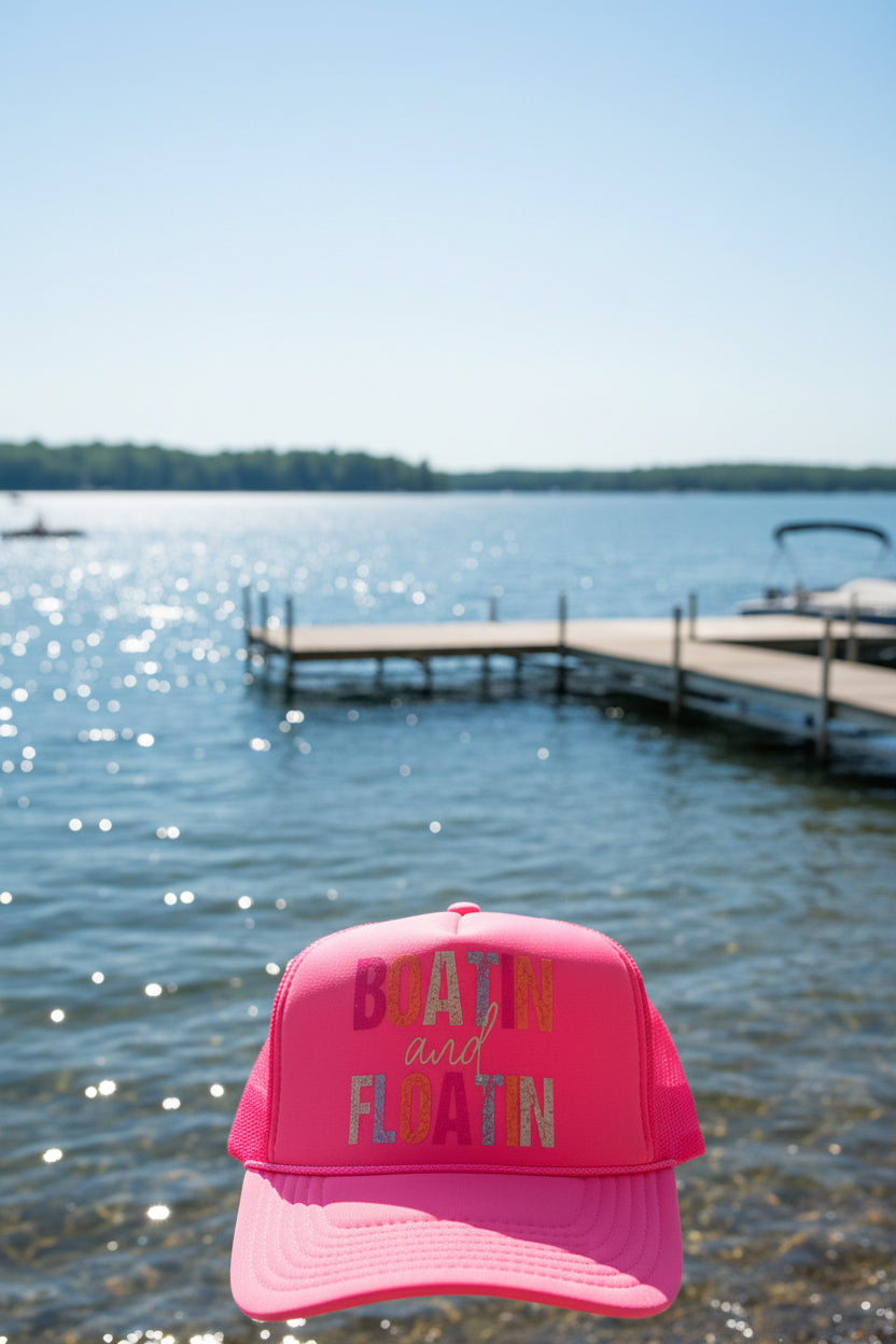 A bright pink trucker hat with a clear vinyl wrap displaying the words 'BOATIN and FLOATIN' in multicolored letters. The hat features an Otto Trucker foam front and mesh back panels.