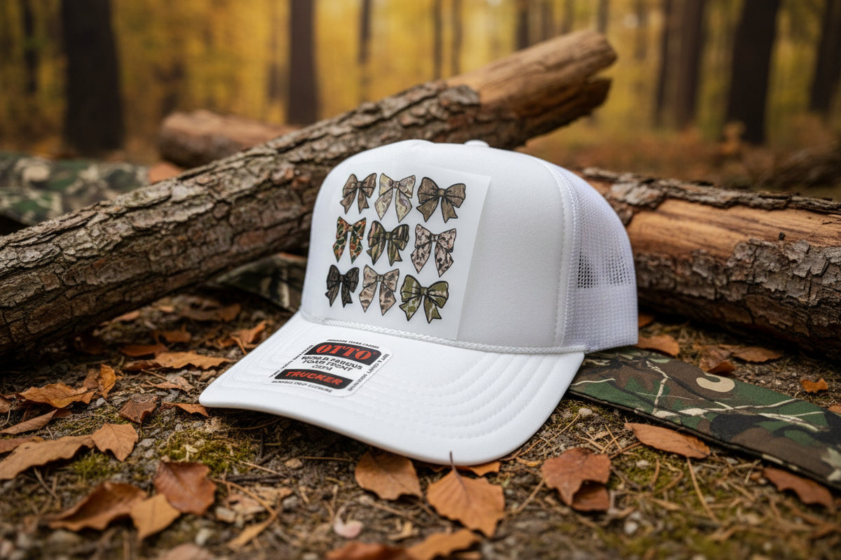 A white trucker hat with a foam front panel, featuring a graphic of twelve camouflage-patterned bow designs on the front. The brim has a visible 'OTFO' brand sticker for 'World Famous Foam Front'.
