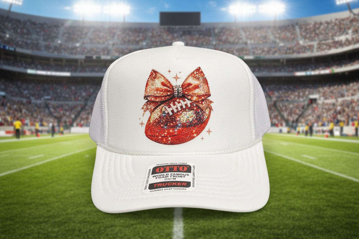A white trucker hat with a glittery red football and bow graphic on the front panel.