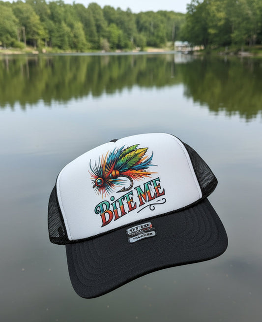 A black and white trucker hat featuring a colorful graphic of a fishing fly with the text 'BITE ME'. The front panel is white with a large graphic, while the mesh back and brim are black.