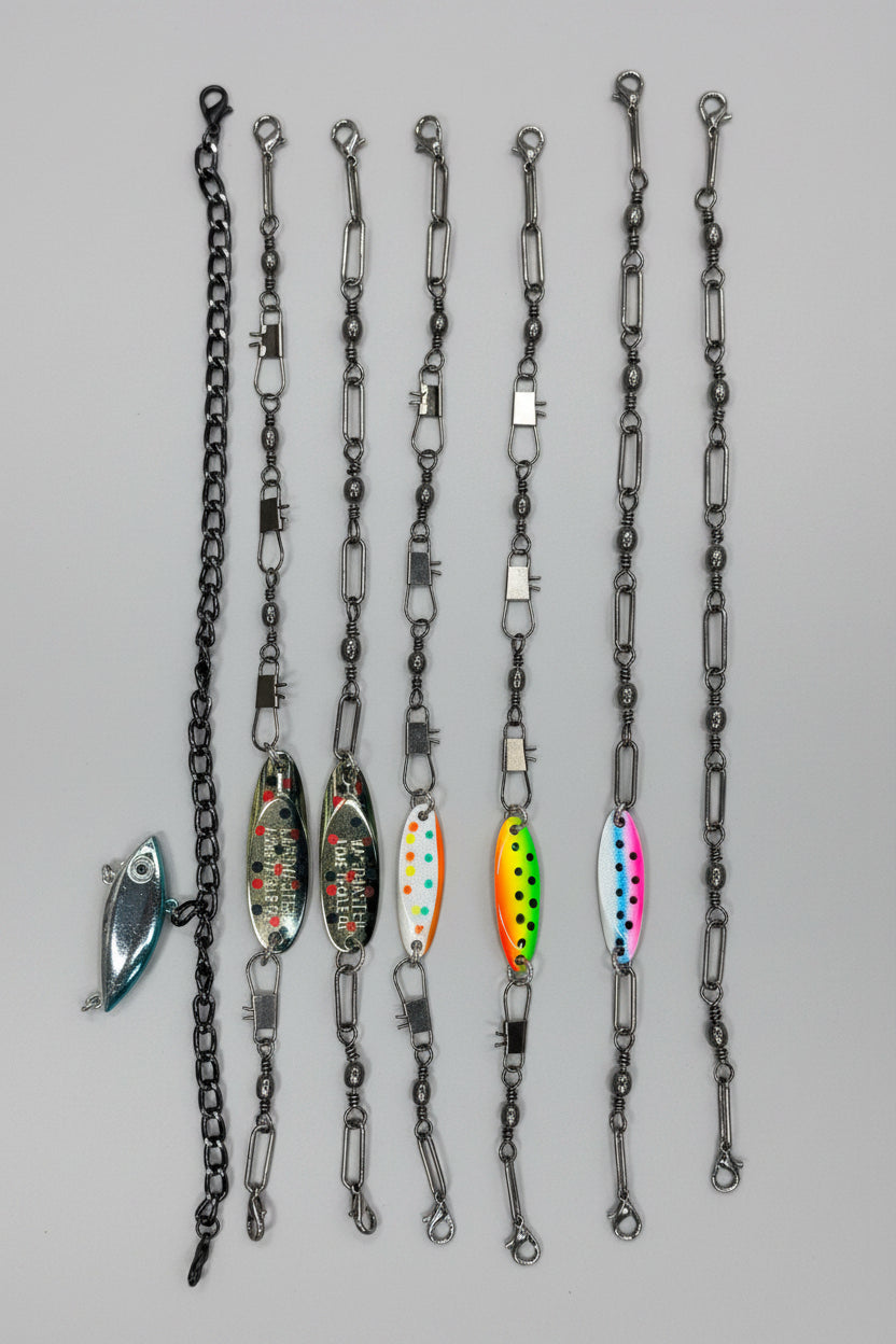 Fishing hat chains with attached dark metal chains are arranged vertically on a light wood surface. The lures include a silver fish-shaped lure, three oval green-and-white patterned lures, and two bright neon lures with pink, orange, yellow, and blue details.