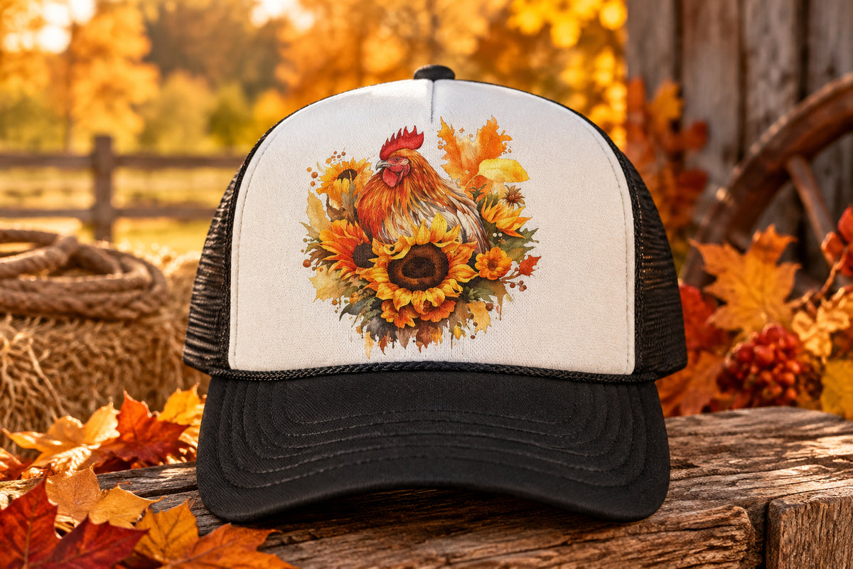 A black and white trucker hat with a colorful watercolor graphic of a rooster and sunflowers on the front panel, resting on a rustic wooden surface.