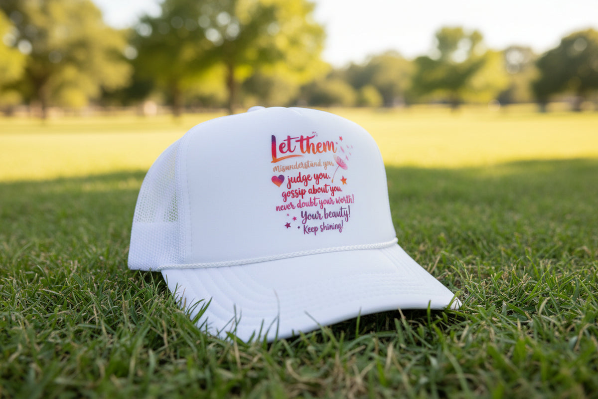 A white trucker hat with a mesh back and a printed graphic on the front. The graphic features the text 'Let them misunderstand you judge you gossip about you never doubt your worth! Your beauty! Keep shining!' in pink, orange, and purple lettering with small decorative doodles.