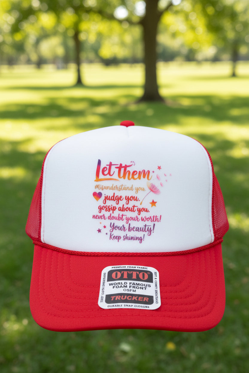 A red and white trucker hat with a printed motivational quote on the front panel and an 'OTTO' brand sticker on the brim, shown on a wooden surface.