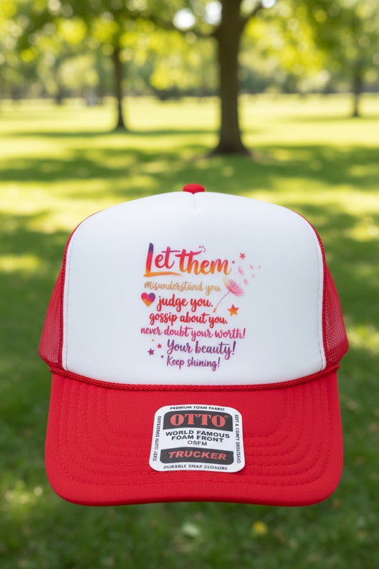 A red and white trucker hat with a printed motivational quote on the front panel and an 'OTTO' brand sticker on the brim, shown on a wooden surface.
