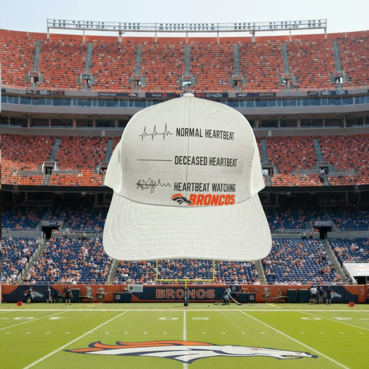 A white baseball cap with black and orange text and a heart monitor graphic, shown floating over a large football stadium with the Denver Broncos logo on the field.