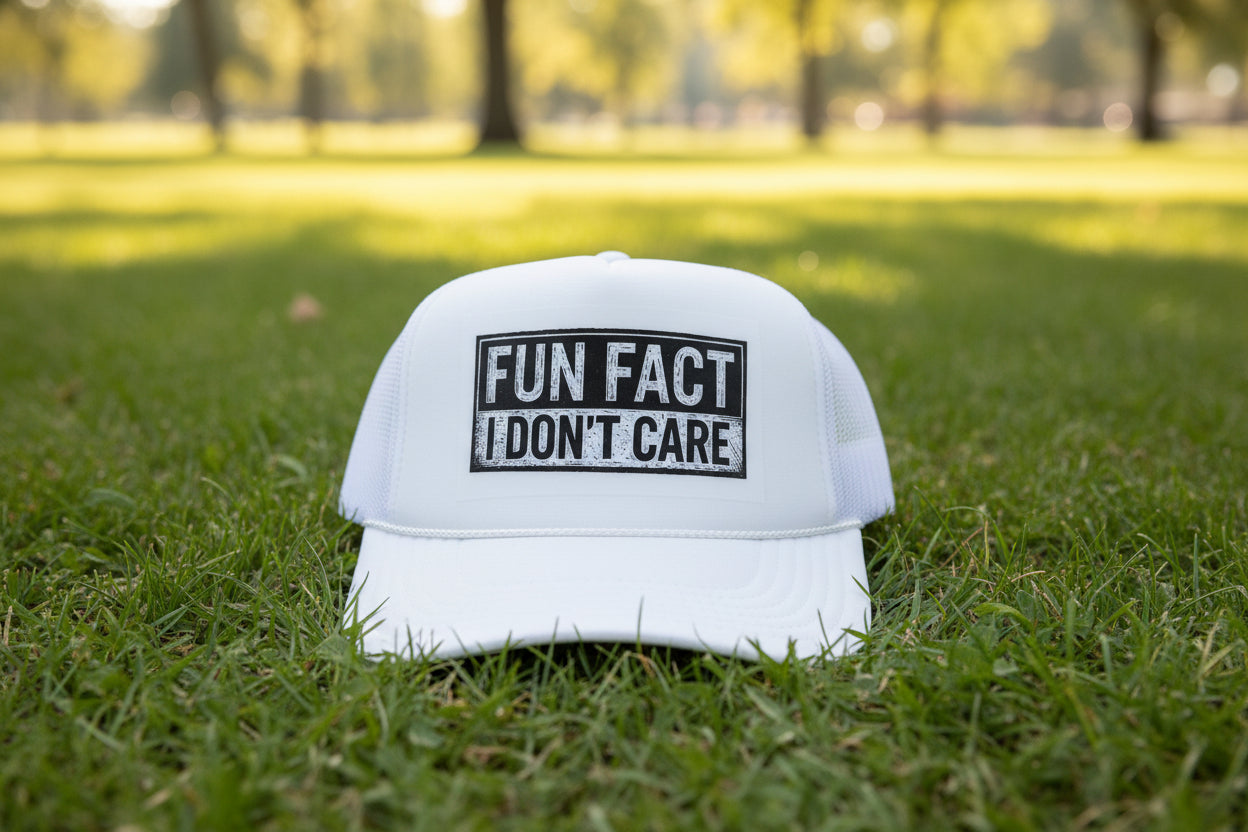 A white trucker hat with a black rectangular patch reading 'FUN FACT I DON'T CARE' and a smaller 'OTTO TRUCKER' patch on the side, resting on a wooden surface.