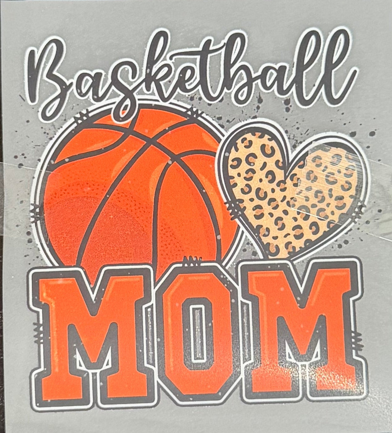 A DTF hat print with a basketball design and the words 'Basketball MOM. The print features an orange basketball, a leopard-print heart, and the word 'MOM' in orange block letters.