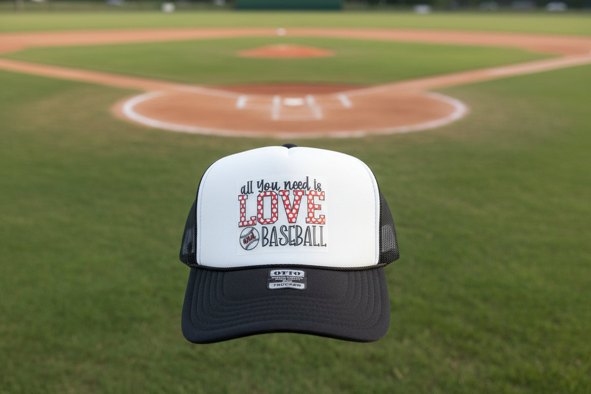A white and black trucker hat with 'all You need is LOVE and BASEBALL' embroidered on the front, resting on a dark wooden surface.