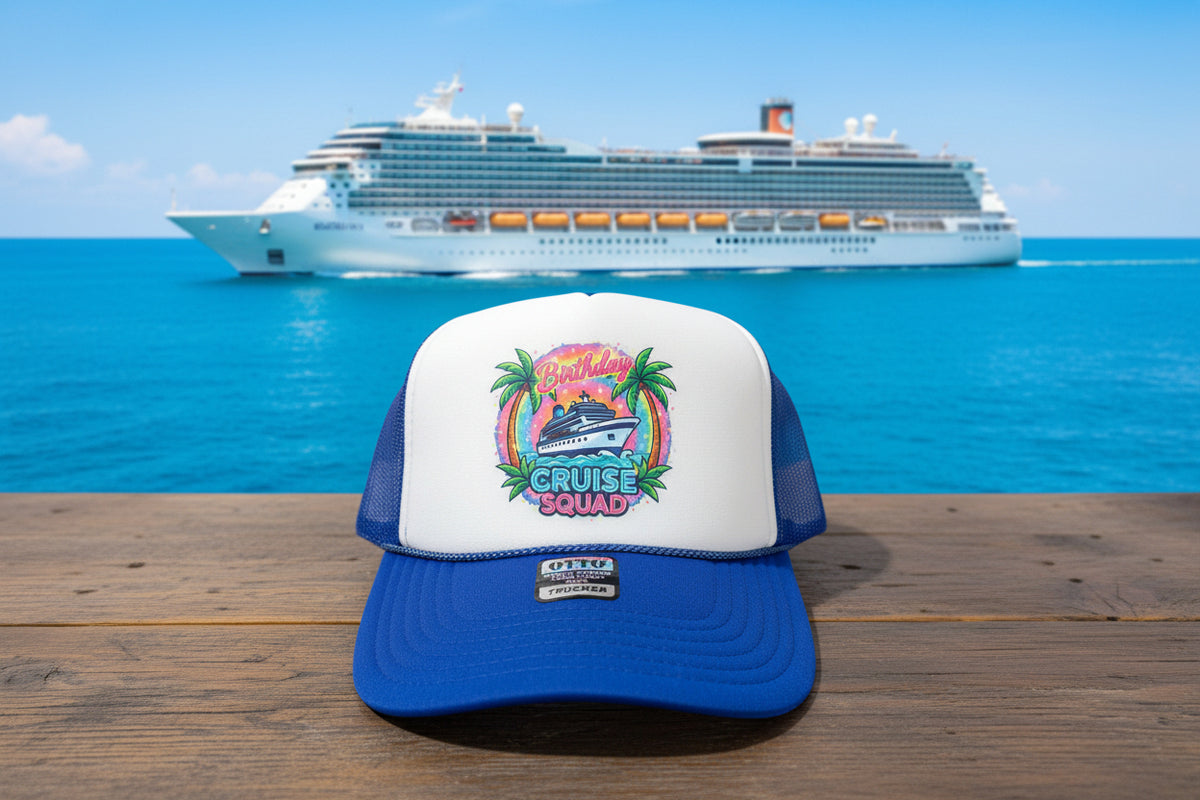 A blue and white trucker hat with a colorful 'Birthday Cruise Squad' graphic on the front, resting on a rustic wooden surface.