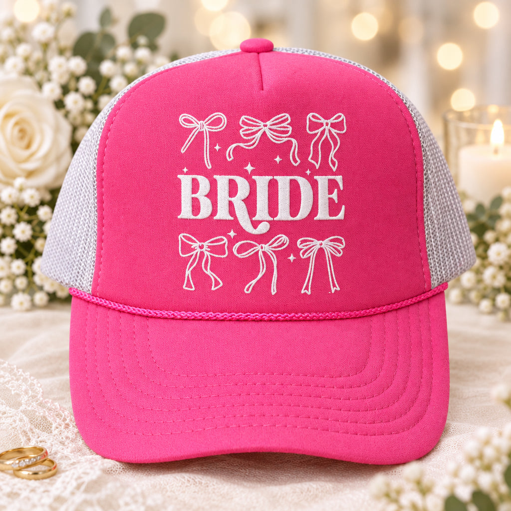 A hot pink and gray trucker hat with 'Bride' printed on the front, displayed on a wooden table.